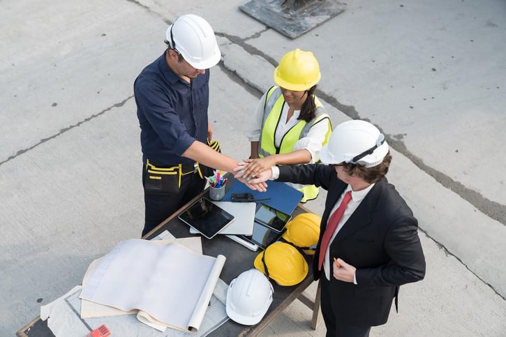 a team involvng the head of a concrete mix corp, an engineer, and a construction worker joining together to complete a project